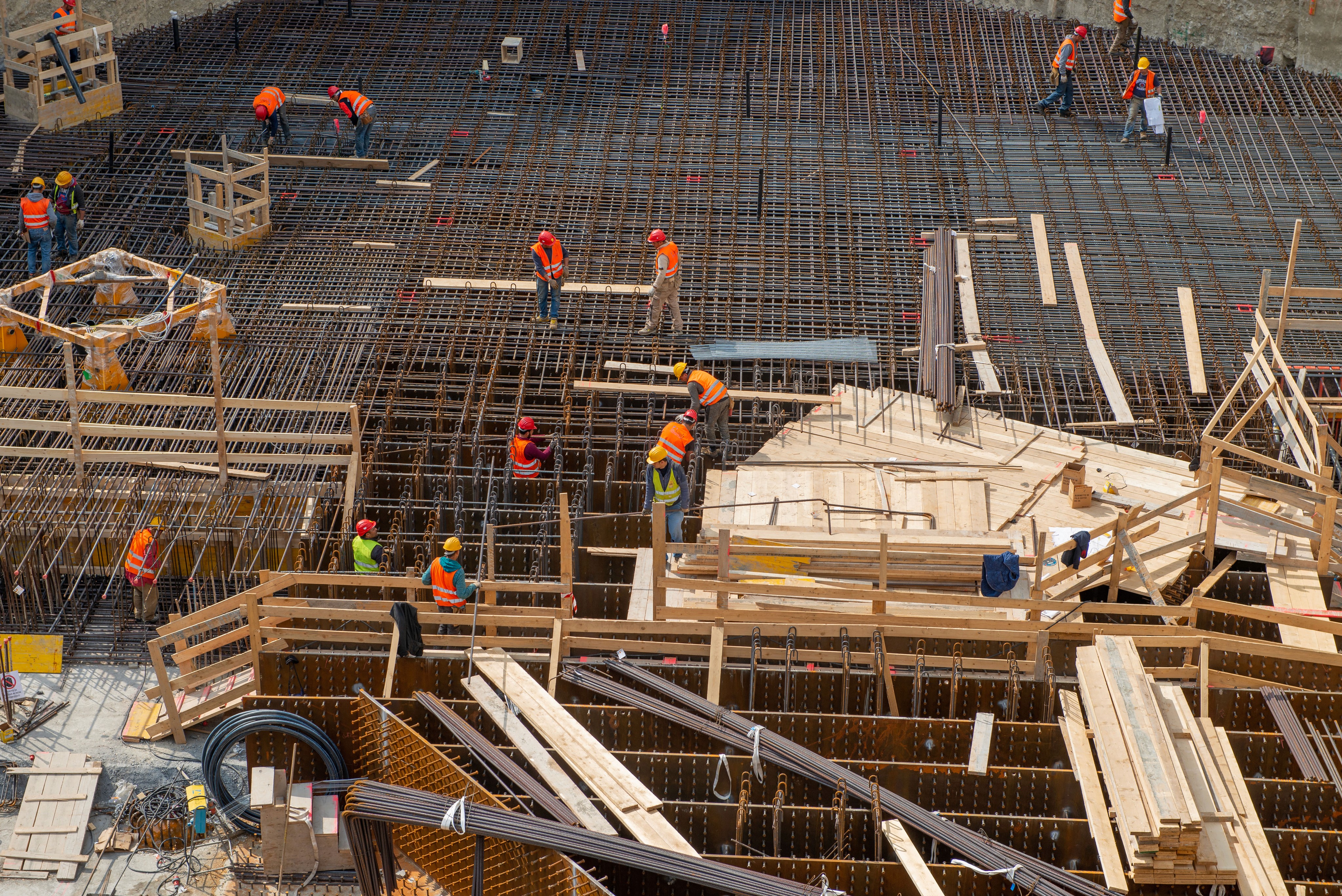 High-angle view of construction workers installing rebar mesh and wooden formwork for a building foundation.