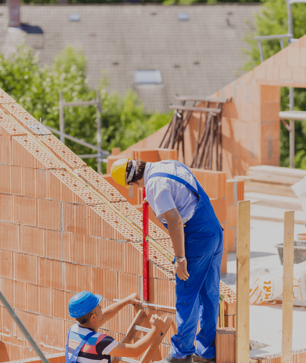 Construction workers wearing hard hats and blue overalls working on a residential brick building site.
